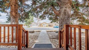Une terrasse en bois qui mène à une maison d’où l’on a une vue dégagée sur la rue et les voitures garées.