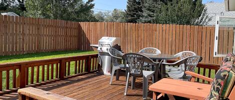 A wooden deck with a grill, outdoor furniture, and a view of a backyard.