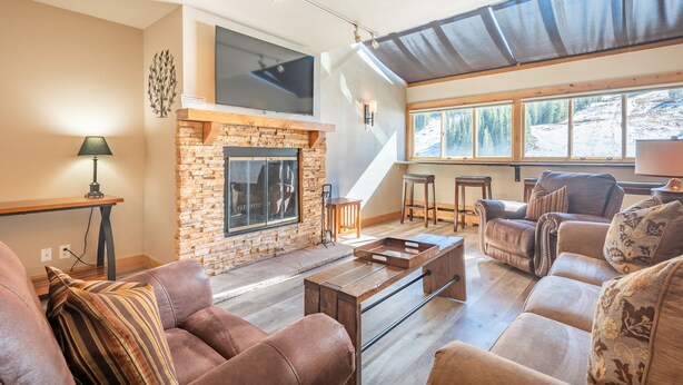 A spacious living room with a stone fireplace, leather sofas, and a large window offering a view of the outdoors.