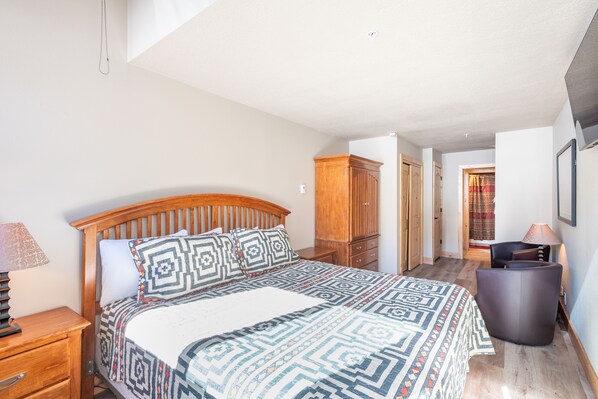 A bedroom with a wooden bed, patterned bedding, a nightstand, a wardrobe, and a chair.