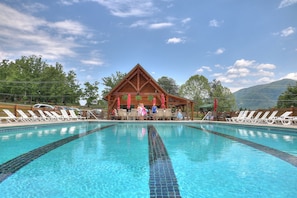 A swimming pool with lounge chairs and a wooden pavilion in the background.