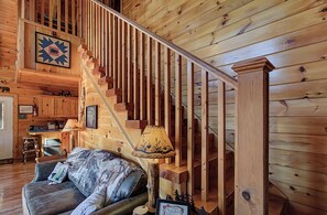 A wooden interior with a staircase, a sofa, a lamp, and a framed picture on the wall.