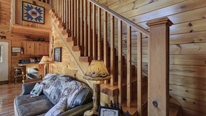 Et interiør i træ med trappe, sofa, lampe og et billede i ramme på væggen.