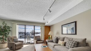 Un soggiorno con divano, poltrona e tavolo, una grande finestra con vista e una lampada a soffitto.