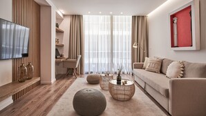 Uma sala de estar moderna com sofá, mesa de centro, puf, TV de tela plana e um espaço de jantar com uma cadeira e mesa.