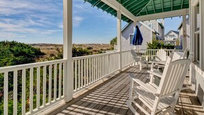 A covered porch with white railings and chairs, overlooking a residential area with houses and a clear sky. - Executive seaside cottage with detached Crofter Cottage. (Bald Head Island)