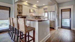 A kitchen with white cabinetry, a central island with bar stools, and a stainless steel refrigerator. - Executive seaside cottage with detached Crofter Cottage. (Bald Head Island)