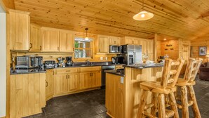 L'intérieur d'un chalet en bois comprend une cuisine équipée de meubles en bois, d'un îlot central avec des tabourets de bar, un four à micro-ondes et un réfrigérateur.