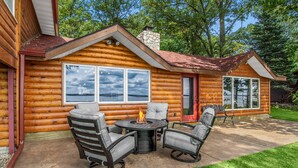 Un chalet en rondins doté d’un patio comprenant un foyer extérieur, des sièges et une vue sur la forêt environnante.