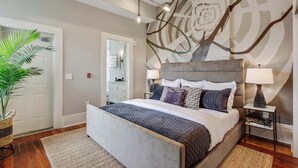 A bedroom with a large bed, bedside tables, a mirror, and a wall with a geometric pattern.