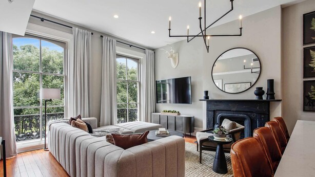 A modern living room with a sofa, a fireplace, a dining table, and a large window with curtains.