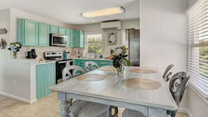 Een keuken met teal kastjes, een wit aanrecht en een eettafel met vier stoelen.