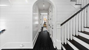 Ein Korridor mit weißen Wandverkleidungen, einem dunklen Holzboden und einer Treppe mit weißen Geländern und dunklen Stufen.