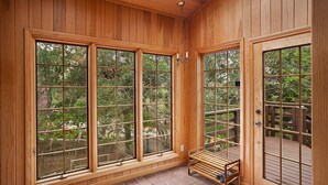 A wooden interior with large windows, a bench, and a door leading to an outdoor deck.
