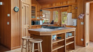 A wooden kitchen with a central island, stools, and a clock on the wall.