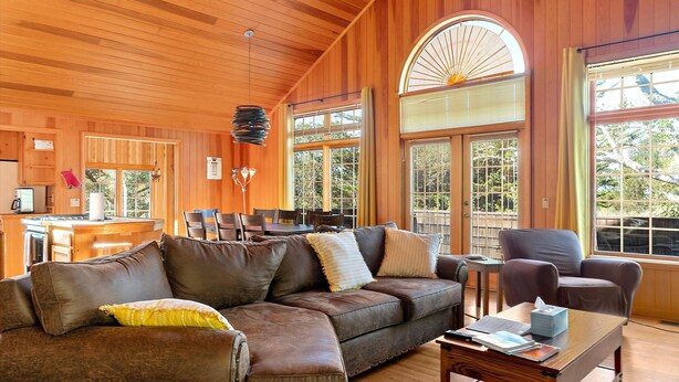 A cozy living room with a brown leather sofa, a wooden coffee table, and a dining area with a kitchen in the background.
