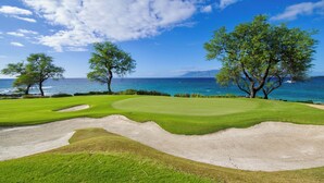 Campo de golf con búnkeres y árboles, con vistas a un cuerpo de agua.