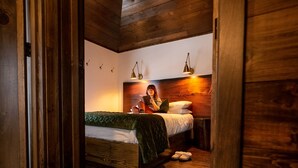 Een houten kamer met een bed, twee wandlampen en een groene deken.