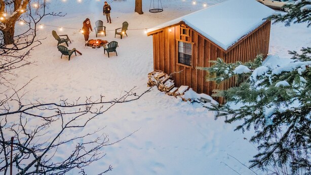 Een gezellig vakantiehuisje met een met sneeuw bedekte dak, omgeven door bomen en lichtjes.