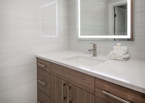 A modern bathroom with a white sink, wooden vanity, and a mirror with built-in lighting.