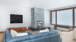 A modern living room with a stone fireplace, a large blue sofa, and a white armchair.