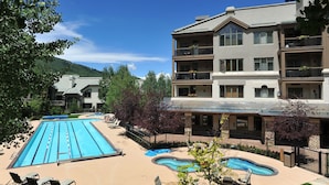 A pool area with lounge chairs, a hot tub, and a building with balconies.
