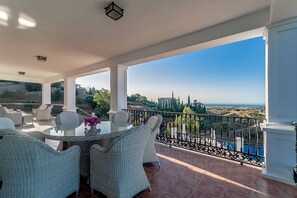A covered outdoor area with a table and chairs, a railing, and a view of the landscape.