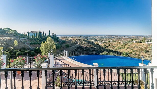 Une piscine offrant une vue dégagée sur le paysage environnant, un balcon avec une balustrade et une vue lointaine sur une colline parsemée de bâtiments.