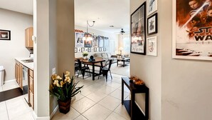 A modern kitchen with wooden cabinets, a dining area with a table and chairs, and a hallway with framed pictures on the walls. - New! Windsor Hills Galaxy's Edge Home, 2mi to Disney!! (Kissimmee)