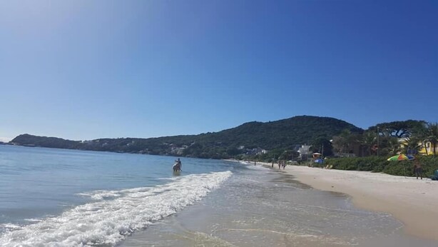 Una playa con aguas azules cristalinas, una orilla arenosa y un paisaje montañoso al fondo.