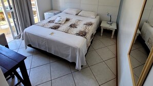 Un dormitorio con cama, mesitas de noche, un espejo y una ventana con cortinas.