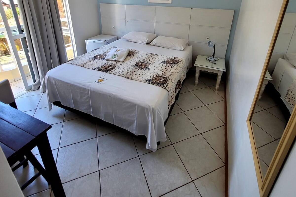 A bedroom with a bed, bedside tables, a mirror, and a window with curtains.