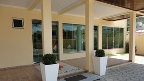 Entrada de un edificio con un patio empedrado, amplias ventanas de vidrio y dos macetas blancas.