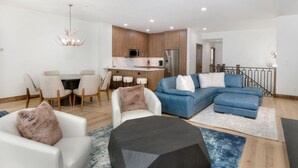A modern living room with a sectional sofa, a dining area with a table and chairs, and a kitchen with wooden cabinets and appliances. - Ski-In & Out Your Doorstep! Lovely Interior, Pool/Hot Tub! (Beaver Creek)