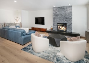 Un salon moderne avec un canapé bleu, des fauteuils blancs, une table basse noire et une cheminée en pierre.