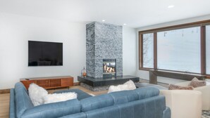 A modern living room with a stone fireplace, a large blue sofa, and a white armchair. - Ski-In & Out Your Doorstep! Lovely Interior, Pool/Hot Tub! (Beaver Creek)