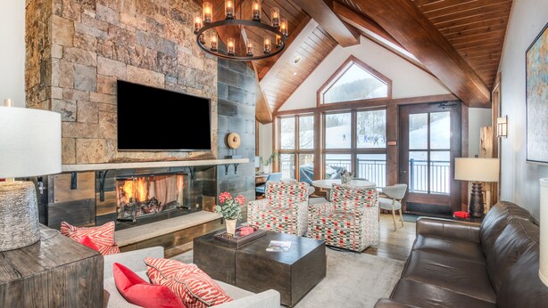 A spacious living room with a stone fireplace, comfortable seating, and large windows offering a view of the outdoors. - Ski-In & Out Your Doorstep! Lovely Interior, Pool/Hot Tub! (Beaver Creek)