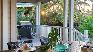 An outdoor dining area with a grill, dining table, chairs, and a tropical garden view.