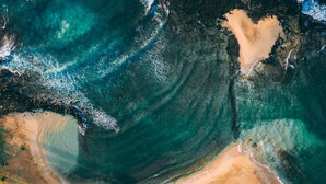 An aerial view of a beach with clear waters, sandy shores, and sparse vegetation.