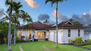 A two-story house with a well-maintained lawn, palm trees, and a garage.