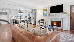 A modern living room with a leather sofa, a fireplace, and a kitchen in the background.