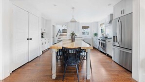A modern kitchen with a central island, white cabinetry, stainless steel appliances, and a wooden floor.