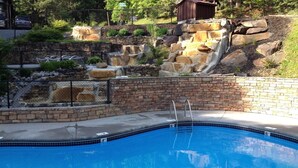 A swimming pool with a stone waterfall feature and a brick wall. - Epic Views, Perfect Location, Fast WiFi (Gatlinburg)