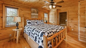 A wooden cabin bedroom with a bed, a ceiling fan, and a window with blinds. - Epic Views, Perfect Location, Fast WiFi (Gatlinburg)