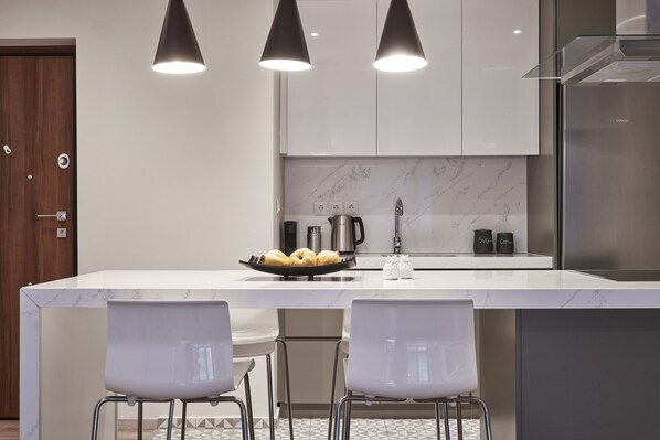 A modern kitchen with a marble countertop, two pendant lights, a Bosch refrigerator, and a coffee maker.