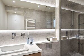 A modern bathroom with a large mirror, a sink, and a glass-enclosed shower.