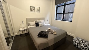 A bedroom with a bed, a nightstand, a lamp, a window, and two framed pictures on the wall. - Large 2 bdrm Flinders St apt on Hosier Lane, with AC. Easy walk to MCG/Aust Open (Melbourne)