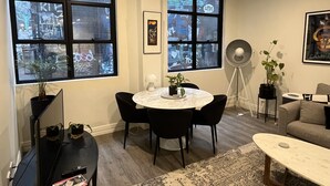 A modern living room with a round table, black chairs, a grey sofa, and large windows offering a view of the city. - Large 2 bdrm Flinders St apt on Hosier Lane, with AC. Easy walk to MCG/Aust Open (Melbourne)