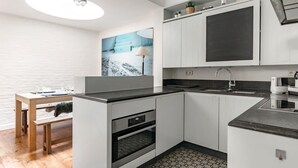 A compact kitchen with white cabinets, a black countertop, a built-in oven, and a tiled backsplash. - Urban Comfort: Central 2-BR Townhouse for 6 (Gent)