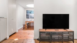 A modern living room with a flat-screen TV mounted on a wooden table, white walls, and a wooden floor. - Urban Comfort: Central 2-BR Townhouse for 6 (Gent)